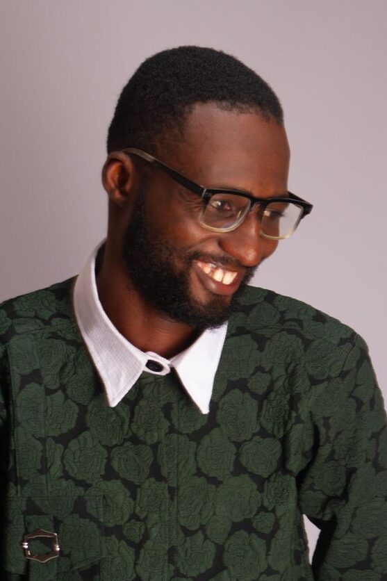 Home Portrait of a smiling young man in a green patterned shirt, exuding confidence and style.