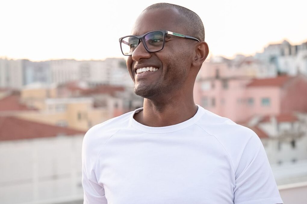 Home African American man smiling in white shirt with cityscape backdrop.